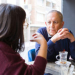 Senior man having a conversation with woman drinking coffee and relaxing, chatting at restaurant